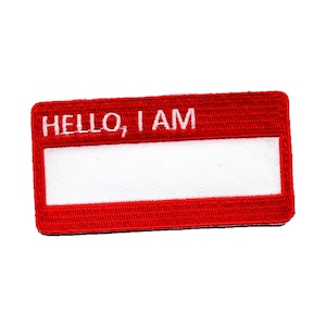 Op de afbeelding: Rode stoffen naamsticker met witte geborduurde tekst die "HELLO, I AM" zegt.