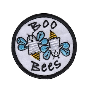 Könnte beinhalten: Ein runder weißer gestickter Aufnäher mit schwarzen Nähten. Der Aufnäher zeigt zwei Cartoon-Geisterbienen mit blauen Flügeln und gelb-schwarz gestreiften Stacheln. Der Text "BOO Bees" ist in Schwarz unter den Bienen geschrieben.
