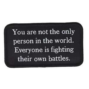 May include: Black rectangular patch with rounded corners. The patch features white embroidered text that reads: "You are not the only person in the world. Everyone is fighting their own battles."