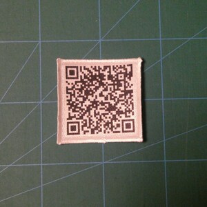 May include: A white fabric patch with a black and white QR code printed on it.
