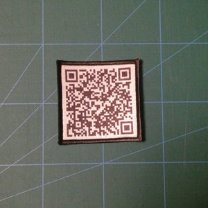 May include: A black and white QR code patch with a black border. The patch is made of fabric and has a white background.