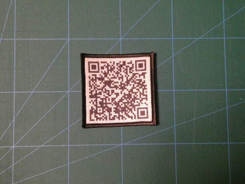 May include: A black and white QR code patch with a black border. The patch is made of fabric and has a white background.