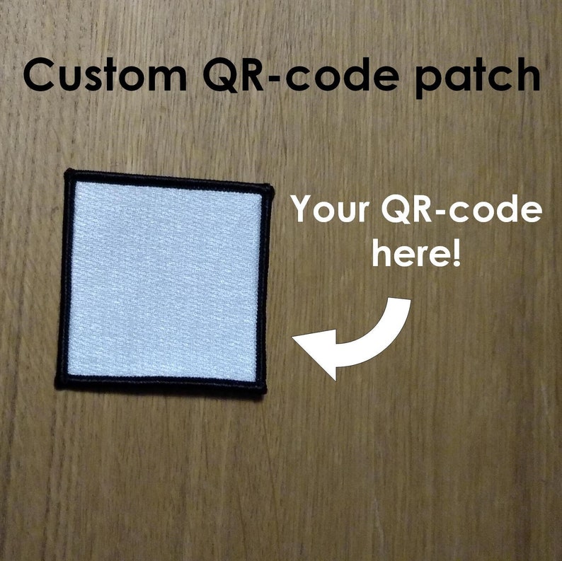 May include: A white square patch with a black border. The patch is made of fabric and has a smooth surface. The text "Your QR-code here!" is written in white on a wooden background.