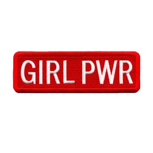 Puede incluir: Parche rectangular rojo con texto bordado en blanco que dice "GIRL PWR".