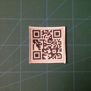 May include: A white fabric patch with a black and white QR code printed on it.