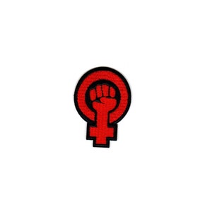 Peut inclure: Patch brodé rouge avec un poing levé à l'intérieur d'un cercle, symbolisant l'autonomisation des femmes. Le poing est à l'intérieur d'un symbole féminin rouge.