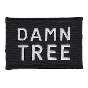 Op de afbeelding: Zwarte geborduurde patch met witte tekst die "DAMN TREE" luidt.