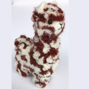 May include: A small, brown and white alpaca figurine made of wool. The alpaca has a fluffy, curly coat and a cute face.