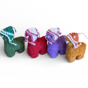 May include: Four colorful, handmade llama figurines. Each llama is a different color: green, red, purple, and brown. They each wear a small, knitted hat with a contrasting color pattern. The llamas are standing on a white surface.