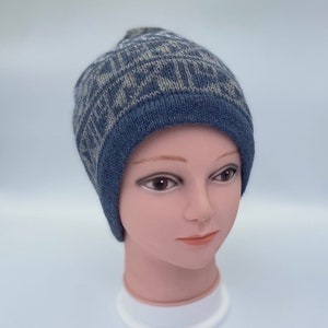 May include: A blue and gray knitted beanie with a patterned design. The beanie is on a mannequin head.