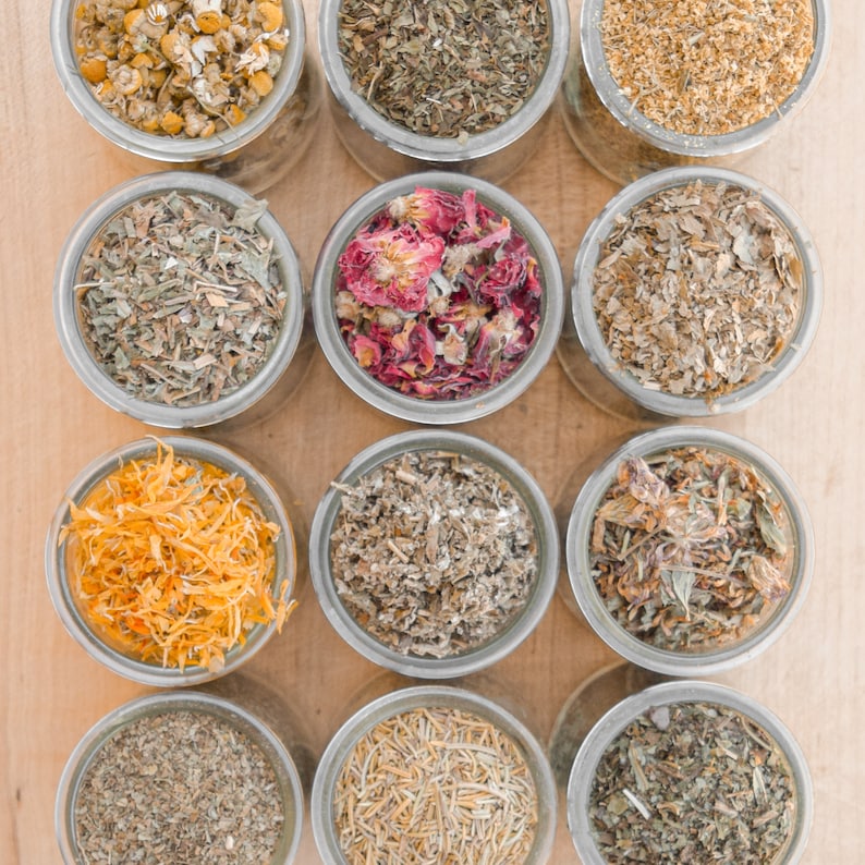 twelve assorted dried herbs for rabbits sit in jars on top of a cutting board
