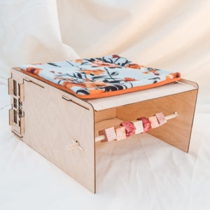 May include: A wooden cat bed with a removable fleece liner and a hanging toy with colorful wooden beads. The bed is made of light wood and has a simple design.