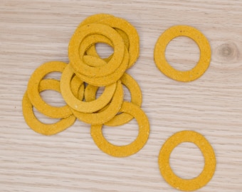 Puede incluir: Un conjunto de arandelas circulares de color amarillo mostaza con una superficie texturizada y mate. Las arandelas están dispuestas en un grupo suelto, con varias superpuestas en el centro y dos anillos separados colocados a la derecha.