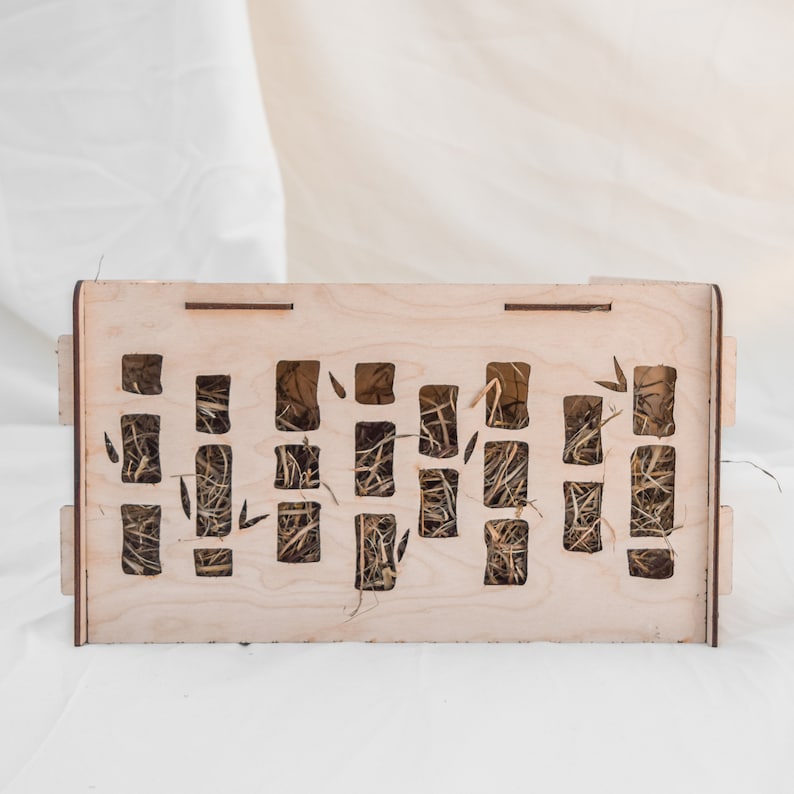 May include: A wooden box with a grid of square openings filled with dried hay. The box is made of light wood and has a natural finish.