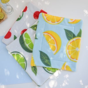 May include: Three fleece pet beds with fruit patterns. One is white with red cherries, another is white with green limes, and the third is light blue with yellow lemons. Each bed has a stitched border and a quilted design.