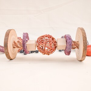 May include: A wooden toy with a woven ball, two wooden blocks, and two purple fabric rings. The toy is designed for small pets to chew on.