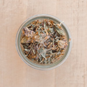 May include: A glass jar filled with dried clover leaves and flowers. The clover is a light brown color and the leaves are a light green color.