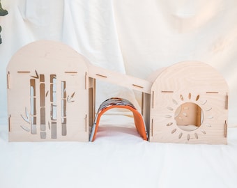 May include: A wooden playhouse for small pets, featuring two connected rooms with cut-out designs. One room has a bamboo design, the other has a sun design. A fabric tunnel connects the two rooms.