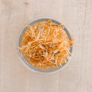 May include: A glass jar filled with dried orange flower petals. The petals are a light orange color and are arranged in a loose, random pattern.