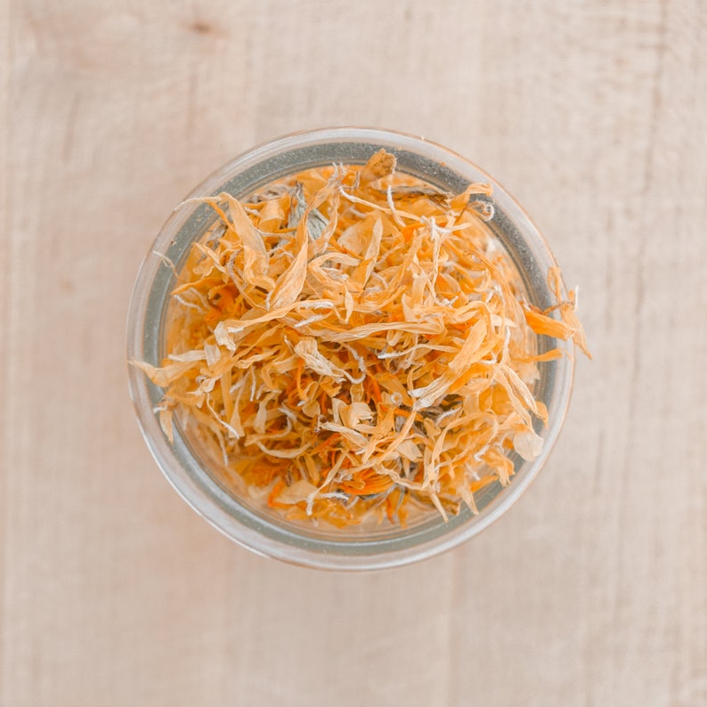 May include: A glass jar filled with dried orange flower petals. The petals are a light orange color and are arranged in a loose, random pattern.