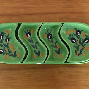 May include: A set of four green ceramic serving dishes with a wavy design. Each dish features a hand-painted floral pattern with black olives and orange accents.