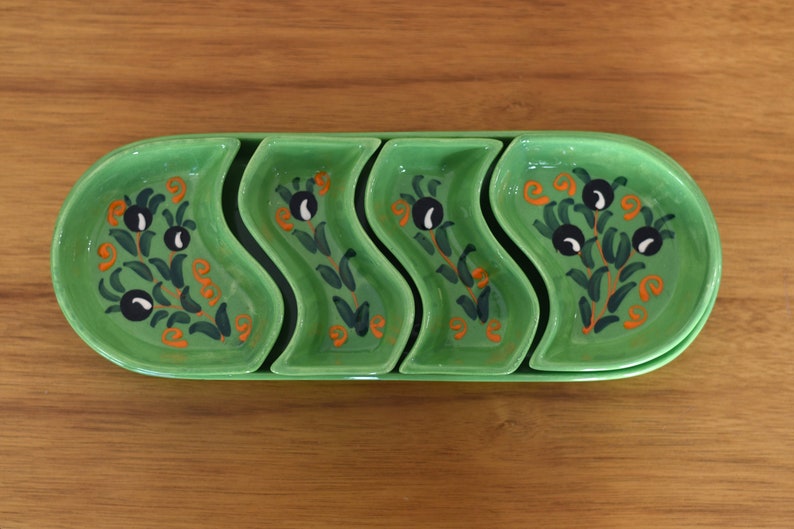 May include: A set of four green ceramic serving dishes with a wavy design. Each dish features a hand-painted floral pattern with black olives and orange accents.