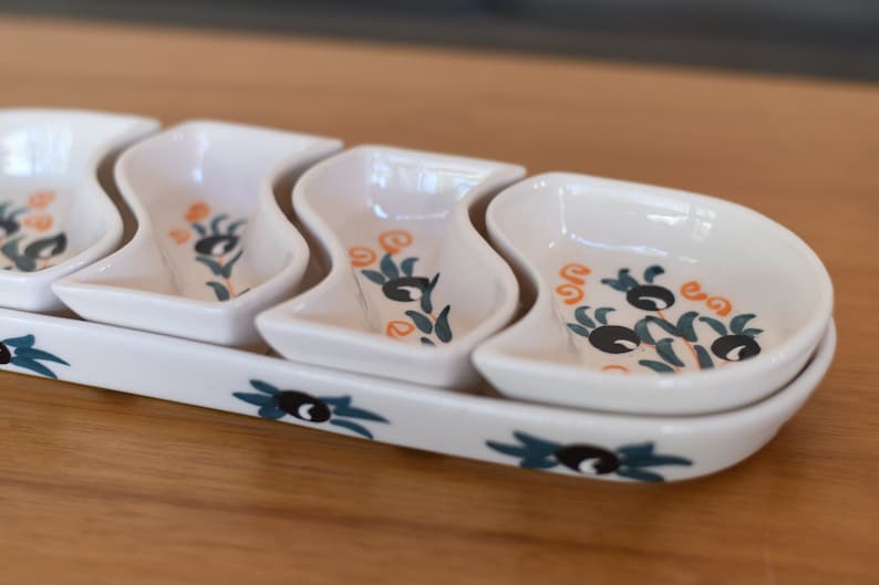 May include: White ceramic serving dish with four individual bowls. The bowls are shaped like a wave and have a green and orange olive branch design.