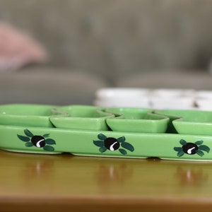 May include: A green ceramic serving dish with four individual bowls. The dish is decorated with black olives and green leaves.