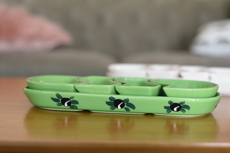 May include: A green ceramic serving dish with four individual bowls. The dish is decorated with black olives and green leaves.