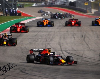 Puede incluir: Un coche de carreras de Fórmula 1 en negro, naranja y rojo, con la palabra "MCLAREN" en el lateral, está conduciendo en una pista de carreras. El coche está en cabeza, con otros coches detrás.