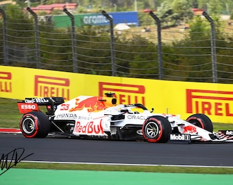 Puede incluir: Un coche de carreras de Fórmula 1 blanco y rojo, con el número 33, corre por una pista. Se ven logotipos de patrocinadores como Pirelli, Honda y Red Bull. Una pancarta amarilla con "IRELLI" está en el fondo.