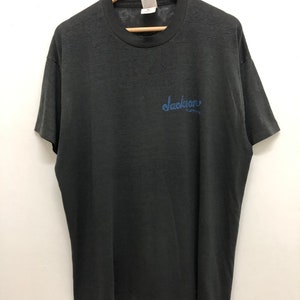 May include: A black t-shirt with a blue embroidered logo that says "Jackson Guitars".