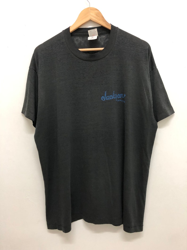 May include: A black t-shirt with a blue embroidered logo that says "Jackson Guitars".