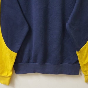 May include: A navy blue sweatshirt with yellow sleeves. The sweatshirt has a crew neck and long sleeves.