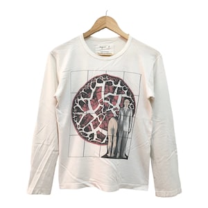 May include: White long-sleeve t-shirt with a graphic print of a person standing in front of a red and black circle with a grid pattern. The text "The Dark Side Of The Moon" is printed on the shirt.