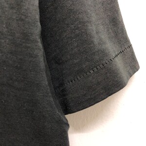May include: Close-up of the black fabric sleeve of a t-shirt. The sleeve is sewn with a zig-zag stitch.
