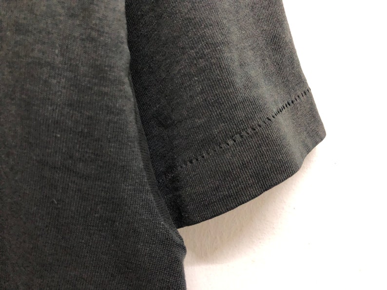 May include: Close-up of the black fabric sleeve of a t-shirt. The sleeve is sewn with a zig-zag stitch.