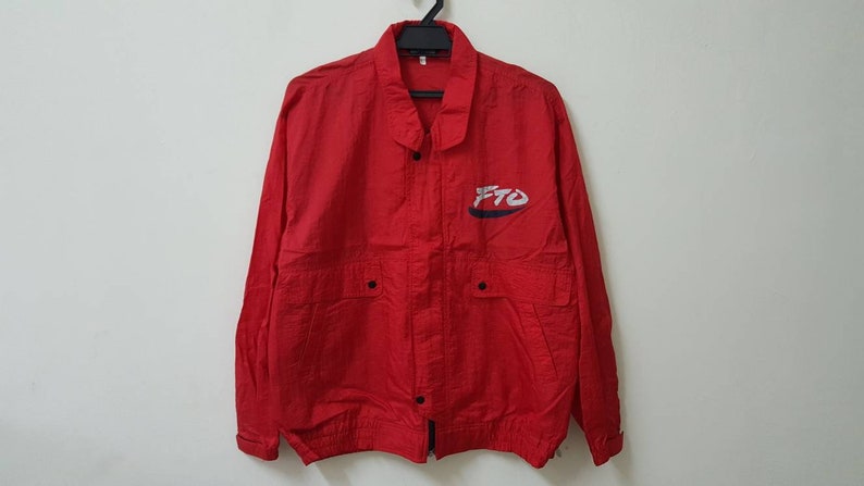 May include: A red windbreaker jacket with a black zipper and snap closure. The jacket has two pockets on the front and a white and blue logo that says "FTO" on the left chest.