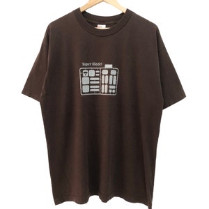 May include: A brown t-shirt with a white graphic of a model airplane and the text "Super Model" printed on the front.
