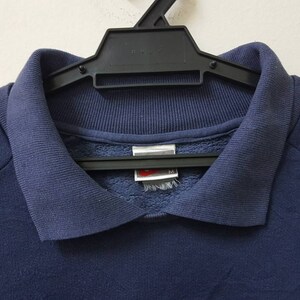 May include: A navy blue sweatshirt with yellow stripes on the sleeves. The sweatshirt has a collared neckline and a small tag on the front.