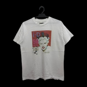 Könnte beinhalten: Weißes T-Shirt mit einem Aufdruck eines Zeitschriften-Covers, das eine Frau zeigt, die zwinkert. Das Zeitschriften-Cover trägt den Text "i-D" und die Zahl "50" in Rot. Das T-Shirt hängt an einem schwarzen Kleiderbügel.