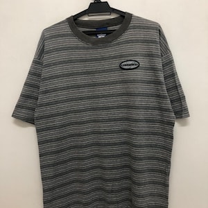 May include: Gray striped t-shirt with a white oval logo that says "UMBRO" in black letters.