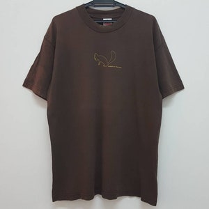 Op de afbeelding: Een bruin T-shirt met een gouden omtrek van een eekhoorn en de tekst "Squirrel Heaven" op de voorkant.