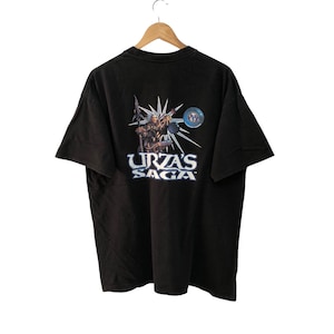 May include: Black t-shirt with a graphic of a character from the Magic: The Gathering card game "Urza's Saga". The graphic features a blue and silver design with the text "Urza's Saga".