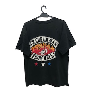 Pode incluir: Camiseta preta com um gráfico nas costas que diz "ICE CREAM MAN FROM HELL" em um design branco, vermelho e laranja. O gráfico inclui uma caveira e chamas, com estrelas vermelhas, brancas e azuis abaixo.