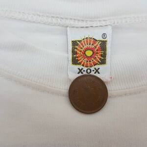 K&ouml;nnte beinhalten: Wei&szlig;es T-Shirt mit einem roten, gelben und orangefarbenen Sonnenstrahlen-Logo mit dem Text "X-O-X" in Schwarz.