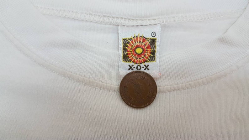 K&ouml;nnte beinhalten: Wei&szlig;es T-Shirt mit einem roten, gelben und orangefarbenen Sonnenstrahlen-Logo mit dem Text "X-O-X" in Schwarz.