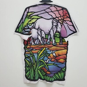 Puede incluir: Camiseta blanca con un estampado de estilo vitral de elefantes y una escena de r&iacute;o. El estampado presenta una variedad de colores, incluyendo verde, azul, morado, naranja y amarillo.