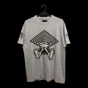 May include: A light gray t-shirt featuring a graphic design of a person falling through a black and white geometric tunnel. The design is centered on the front of the shirt. Small graphic on the left sleeve.