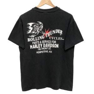 Könnte beinhalten: Schwarzes T-Shirt mit einer weißen Grafik einer geflügelten Figur und dem Text "Rolling Thunder Cycles, Parts & Service for Harley Davidson, 195 Front St., Hempstead, N.Y."